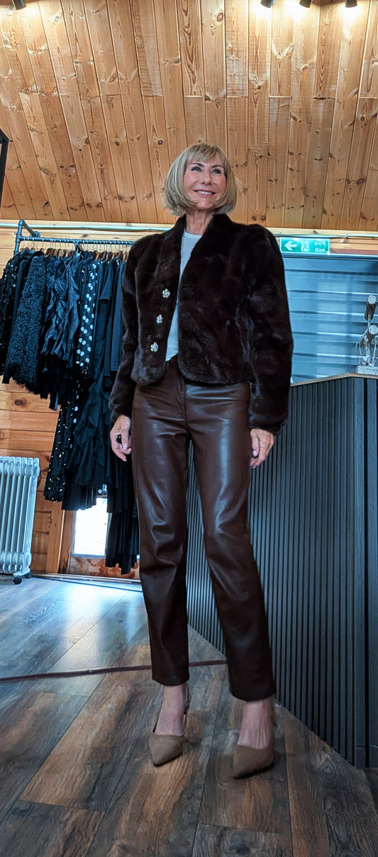 Full-length outfit with Bessie short chocolate faux fur jacket styled over a black top and brown trousers.
