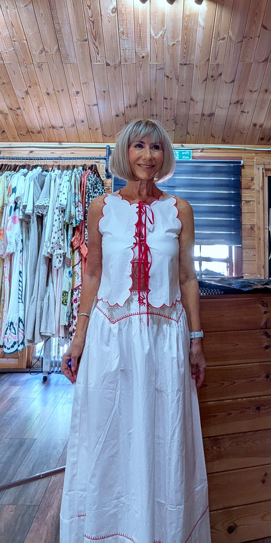 ditsydi UK modelling the Iris white cotton top and matching skirt inside a boutique, featuring red embroidery, scalloped edging and a flowing maxi skirt.