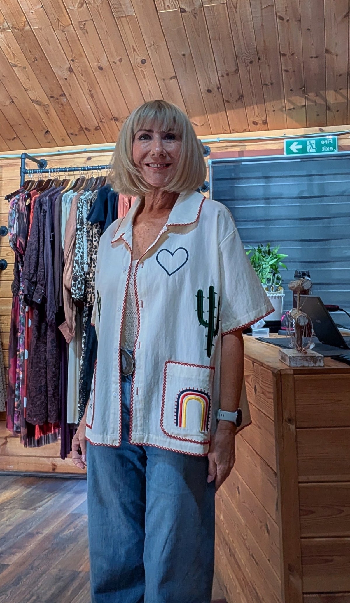 Bernade short-sleeve button-up shirt with embroidered cactus, rainbow, and heart designs, paired with blue jeans.