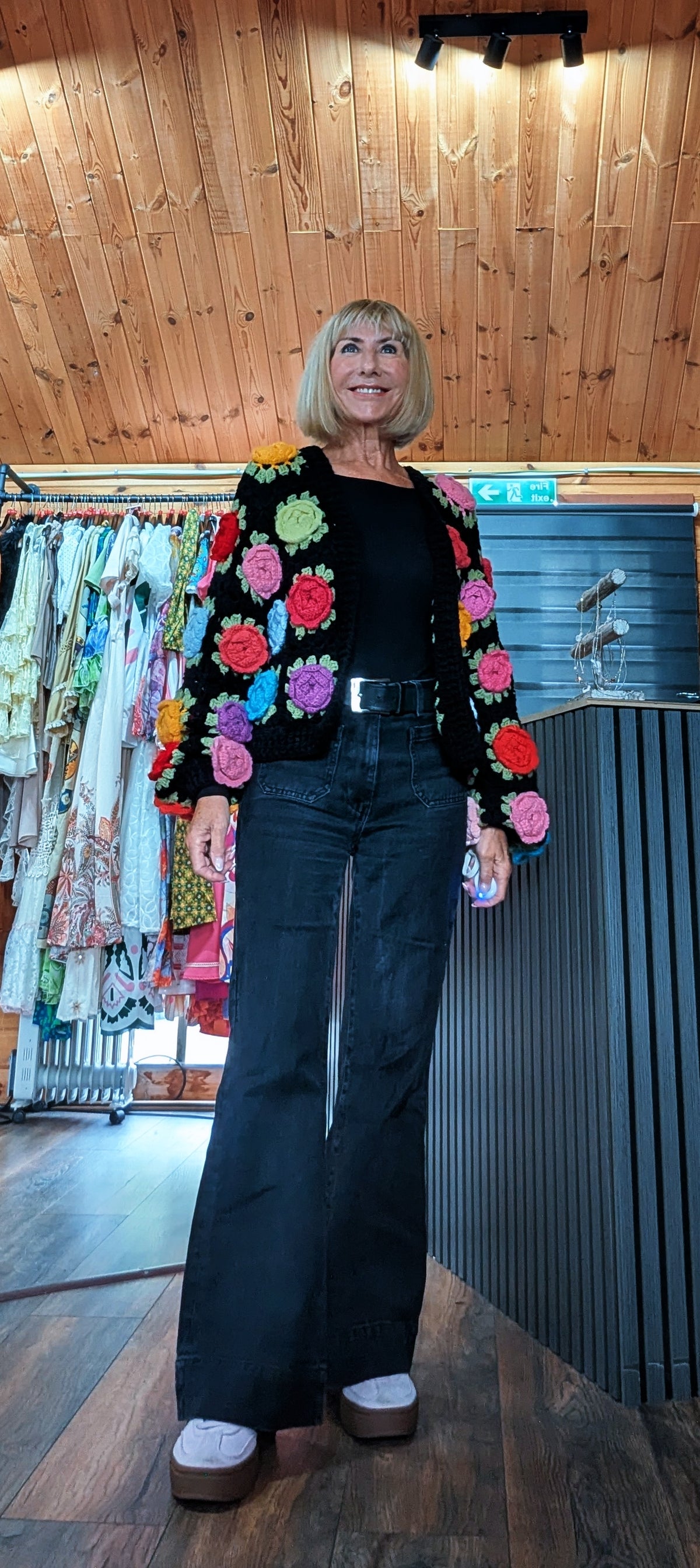 ditsydi wearing Woman wearing the Ora black crochet cardigan with statement 3D flowers with black flared leg jeans
