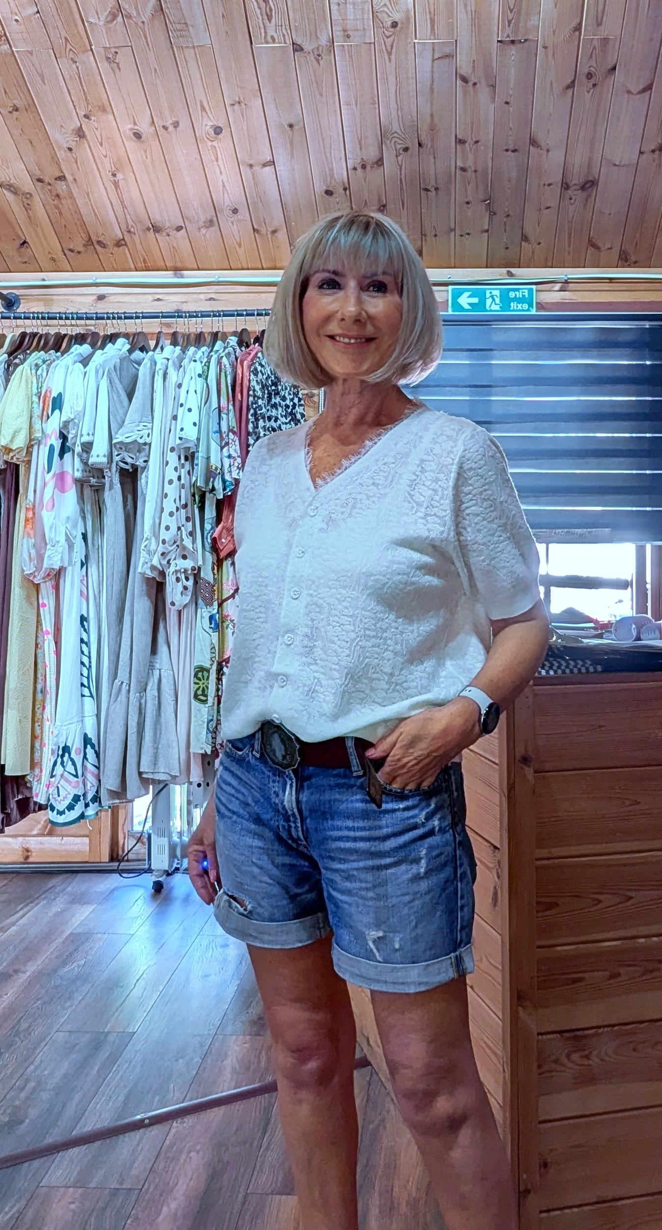 Woman wearing the Adeline cream viscose knit top with a V-neck, button front and short sleeves, styled with denim shorts. One size fits UK 8–14.