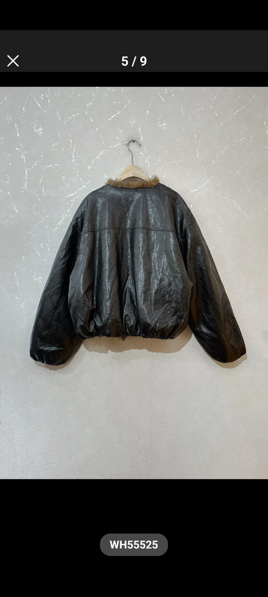 A black faux-leather bomber jacket with a tan faux-fur collar, hanging on a wooden hanger against a textured off-white wall.