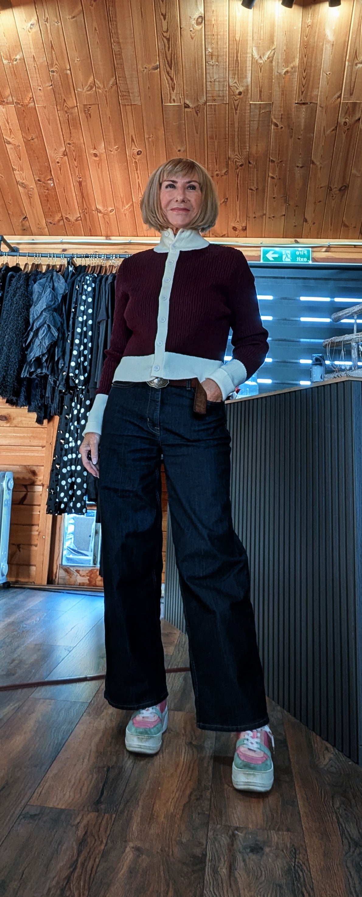 Mallory burgundy cardigan styled with one hand in a jean pocket, showing its cream hem and cuffs