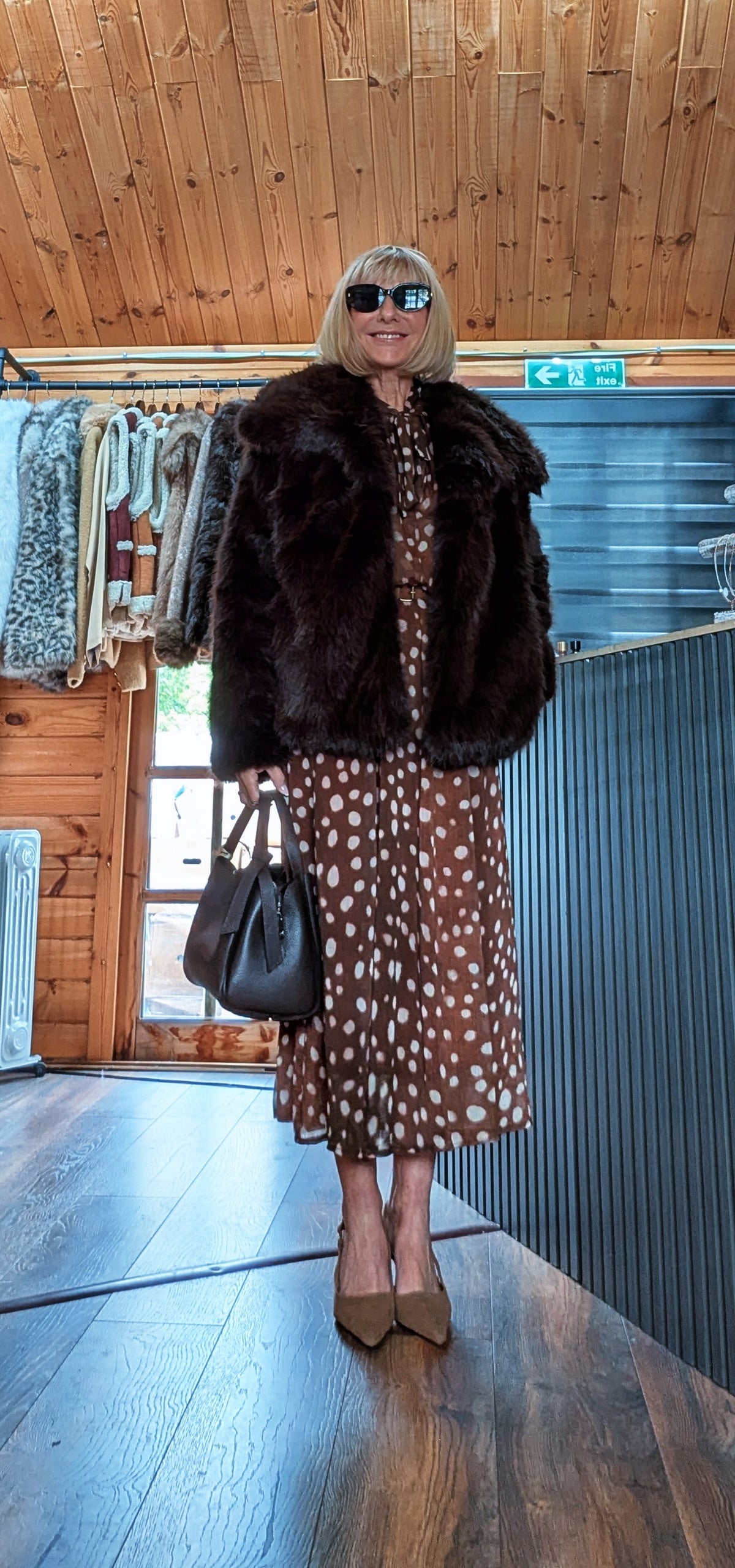 Bella chocolate faux fur jacket worn open over a brown spot-print midi dress with sunglasses and a black handbag
