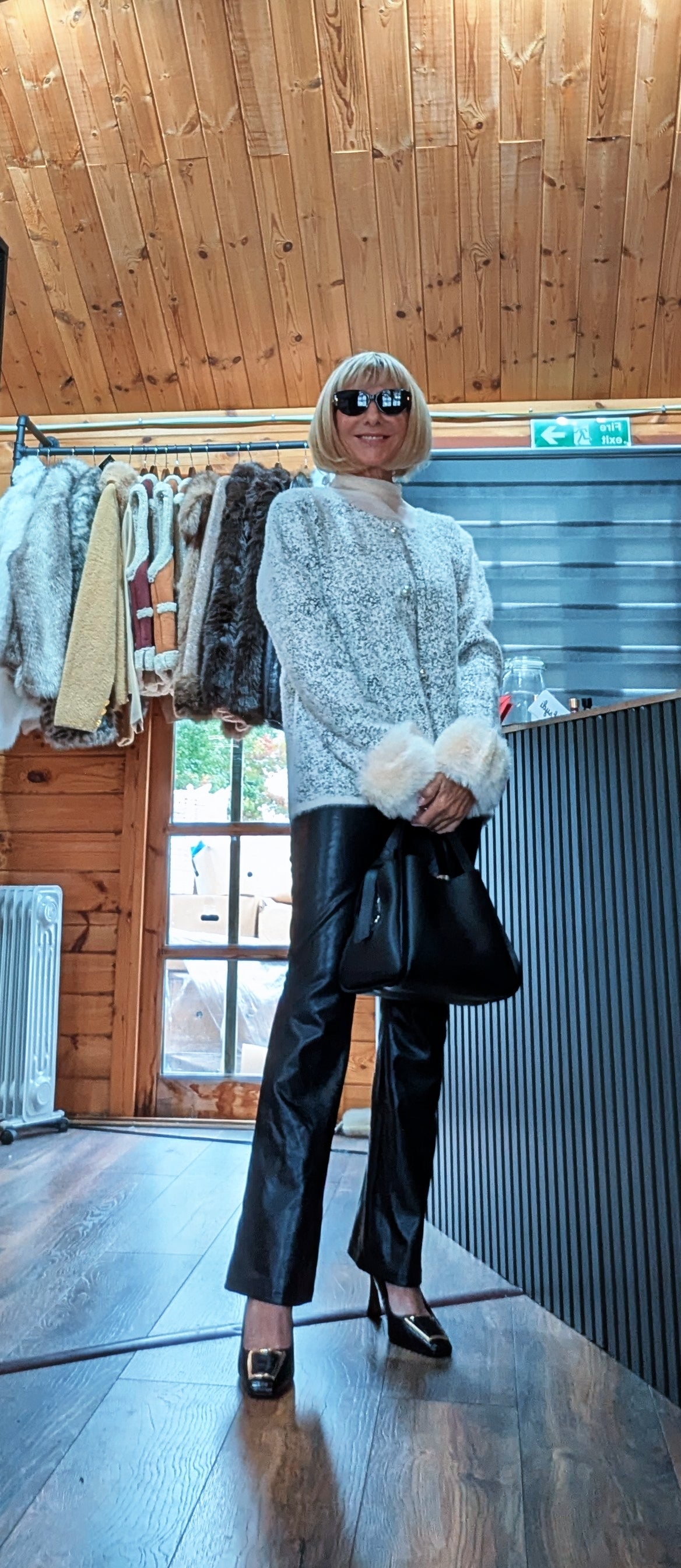 Liv white cardigan styled with sunglasses, black trousers and a black handbag held in front