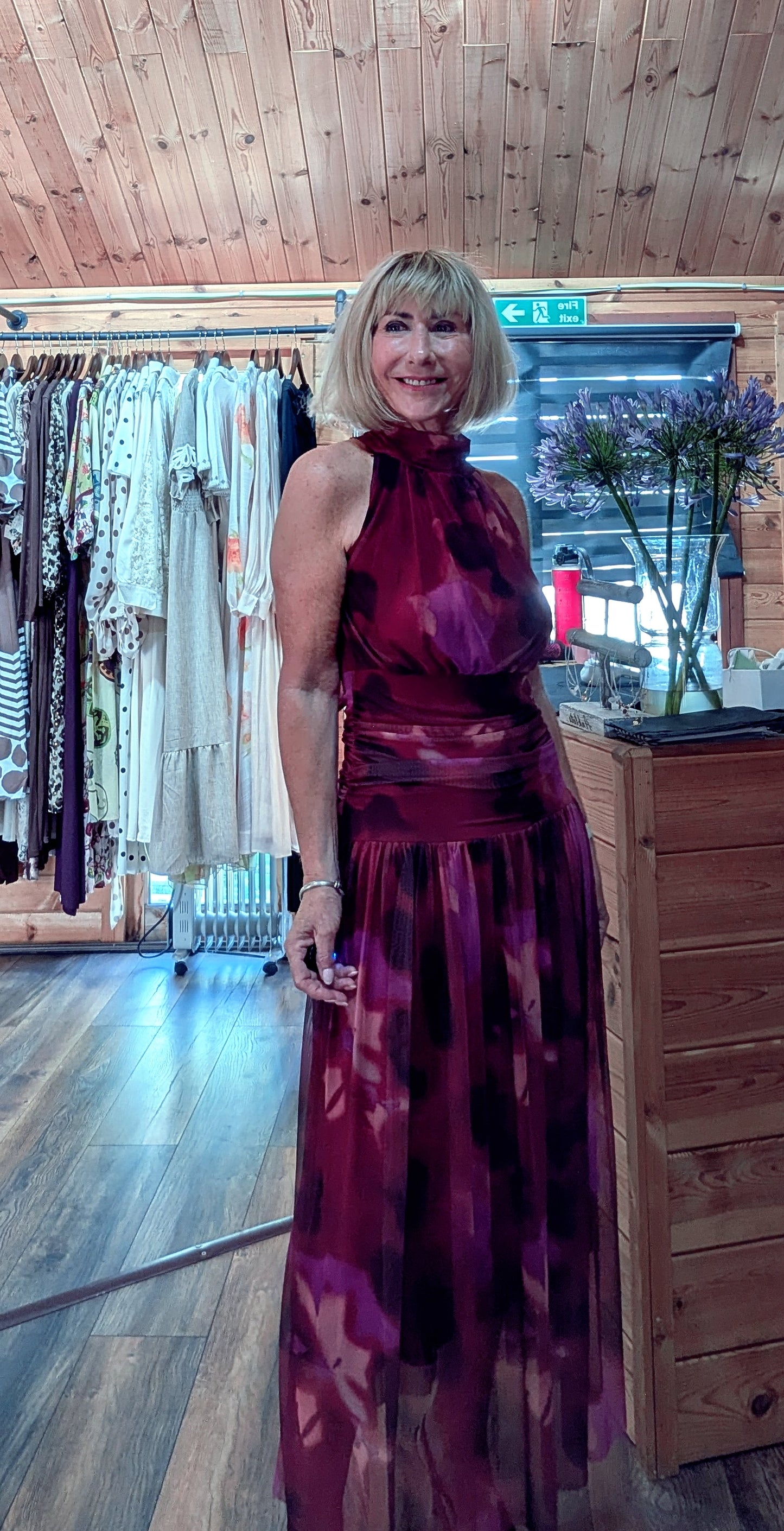 A woman wearing a sleeveless, high-neck, floor-length halter dress in a deep fucshia and purple floral pattern for Autumn  special occasions