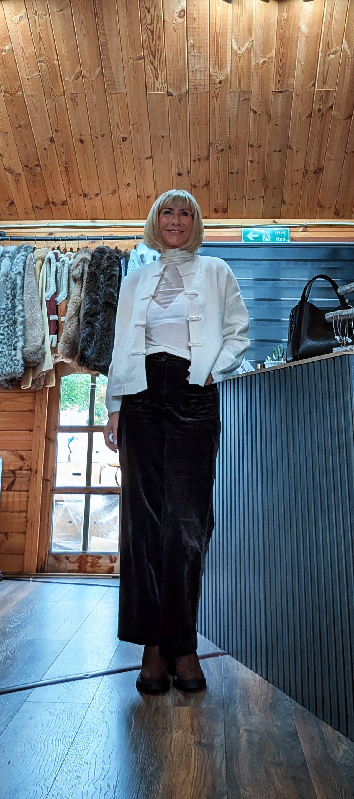 Fran cream knit cardigan worn open at the lower front with one hand in a trouser pocket
