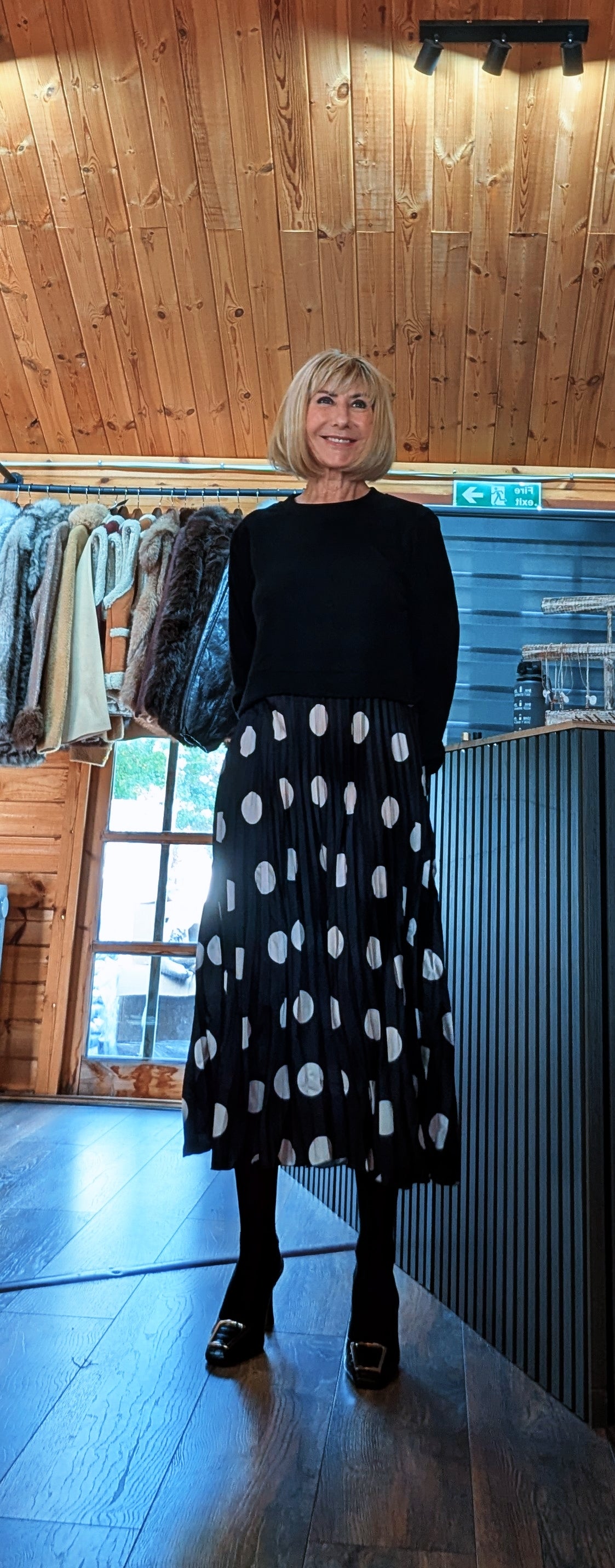 Full-length front view of the Hettie dress with its relaxed black top and spotted midi skirt.