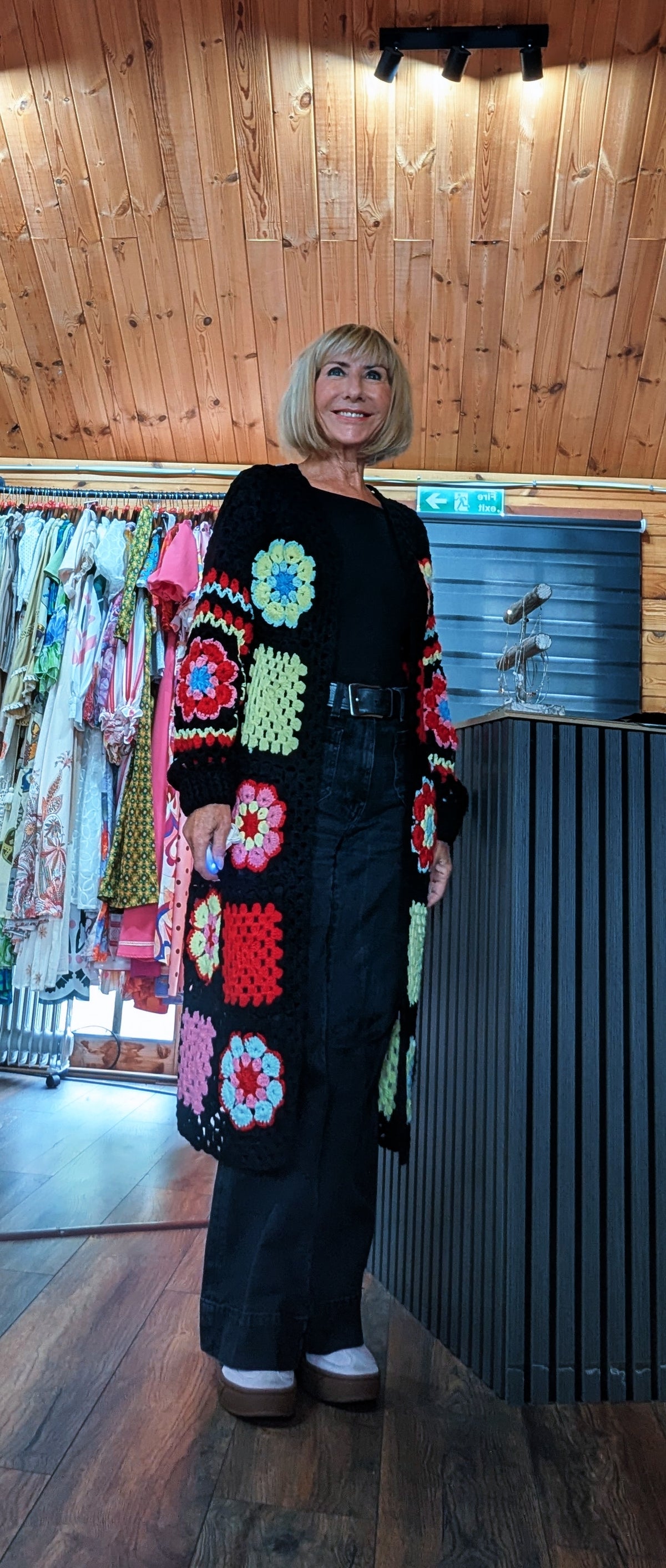 Woman wearing the Fia colourful crochet flower cardigan with a black top and trousers 
