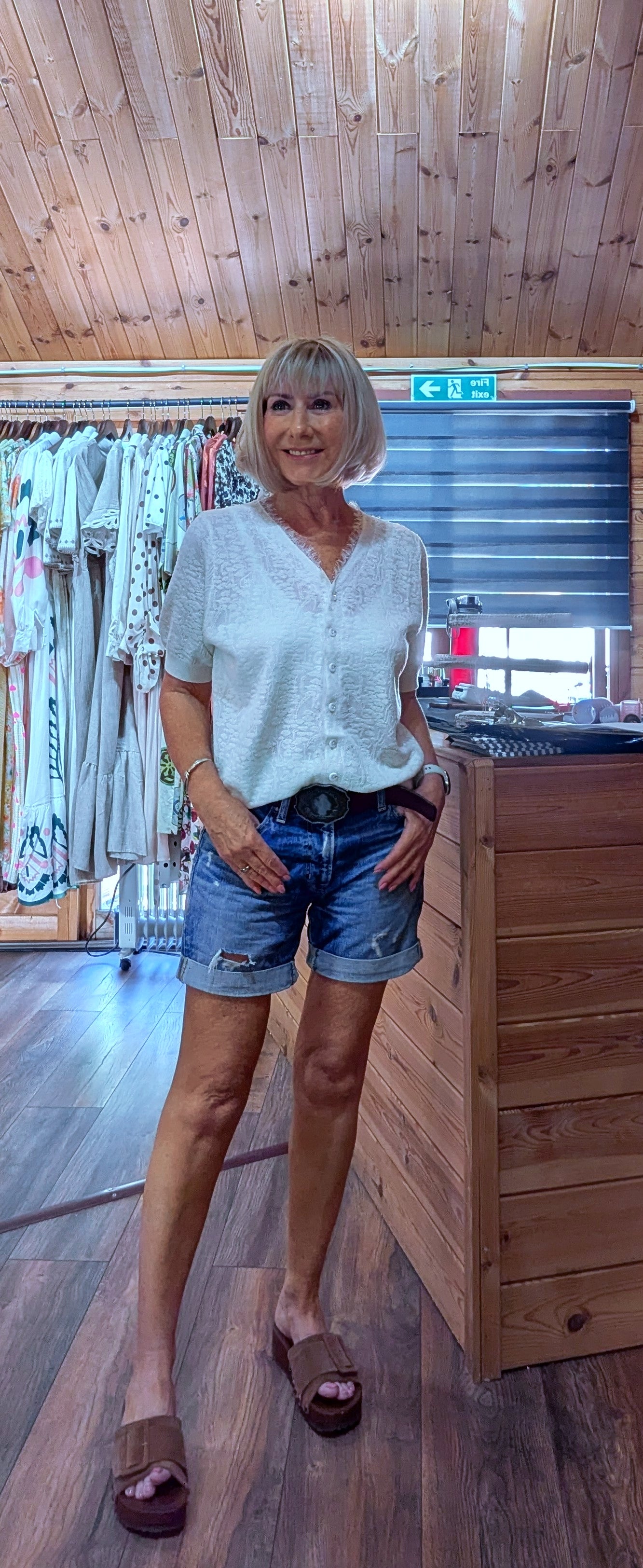 Woman wearing the Adeline cream viscose knit top with a V-neck, button front and short sleeves, styled with denim shorts. One size fits UK 8–14.