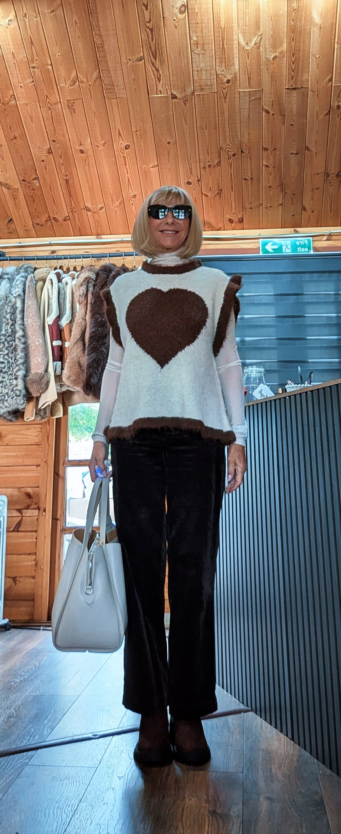 Maura beige and chocolate heart sweater worn with sunglasses and a light-coloured handbag