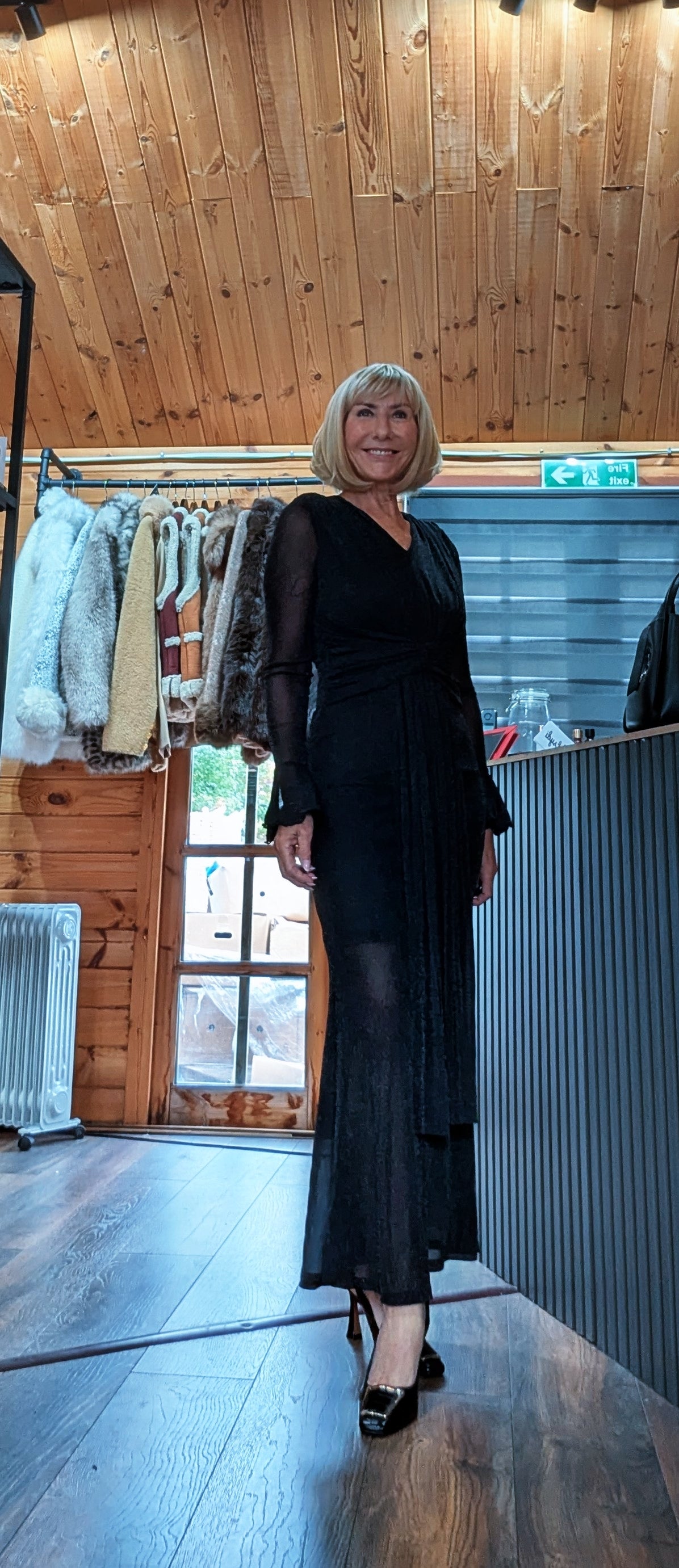 Angled full-length view of Shirley black draped mesh dress worn with black heels