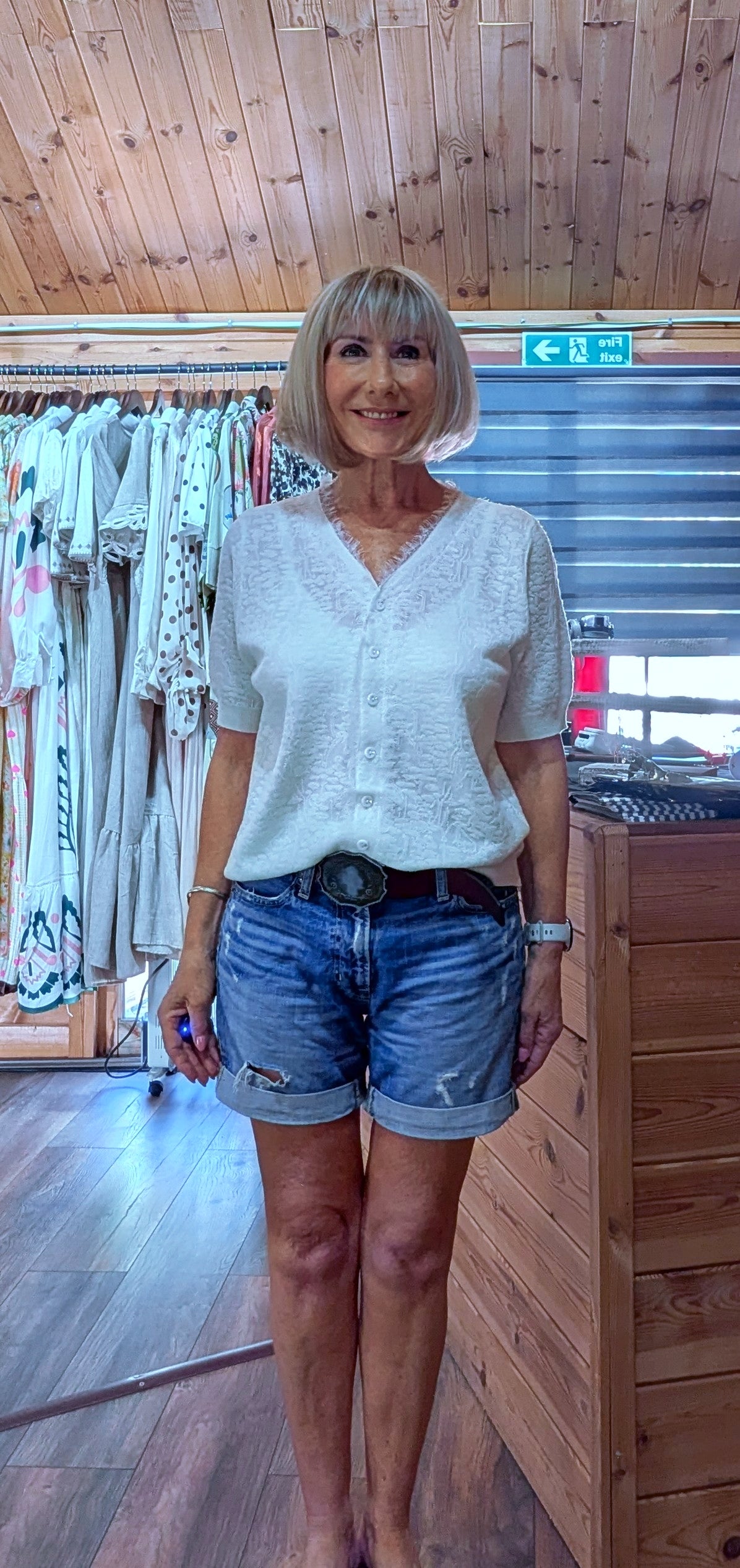 Close up Woman wearing the Adeline cream viscose knit top with a V-neck, button front and short sleeves, styled with denim shorts. One size fits UK 8–14.