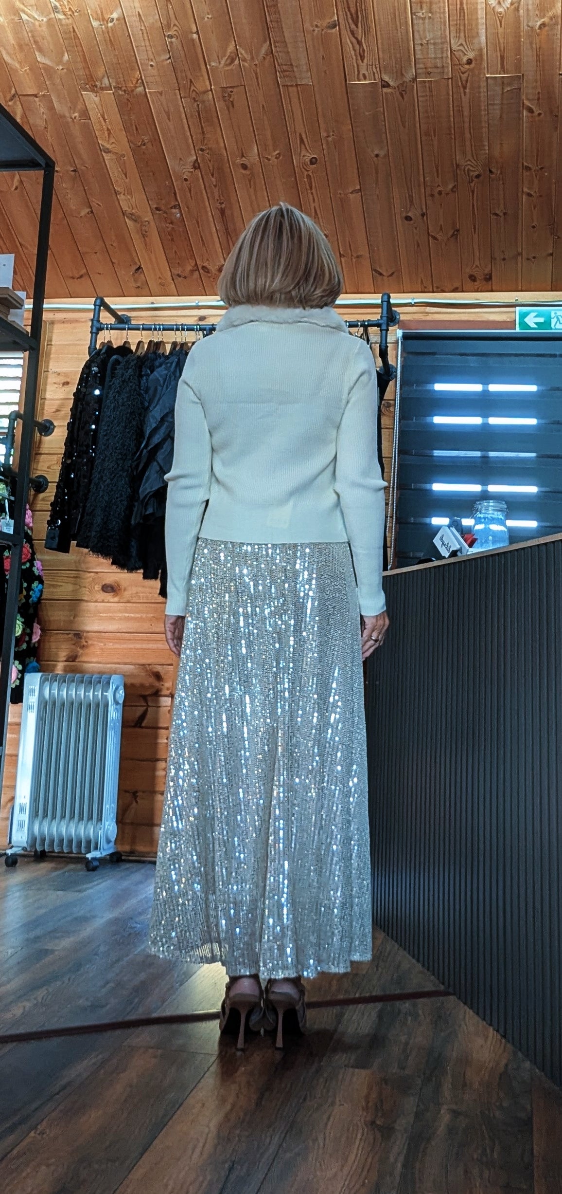 Back view of Cher champagne sequin skirt styled with a cream knit top and heels