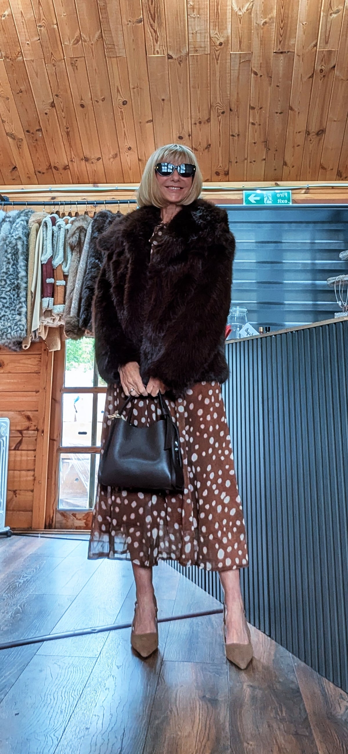 Bella chocolate faux fur jacket modelled with sunglasses and a black handbag held in front