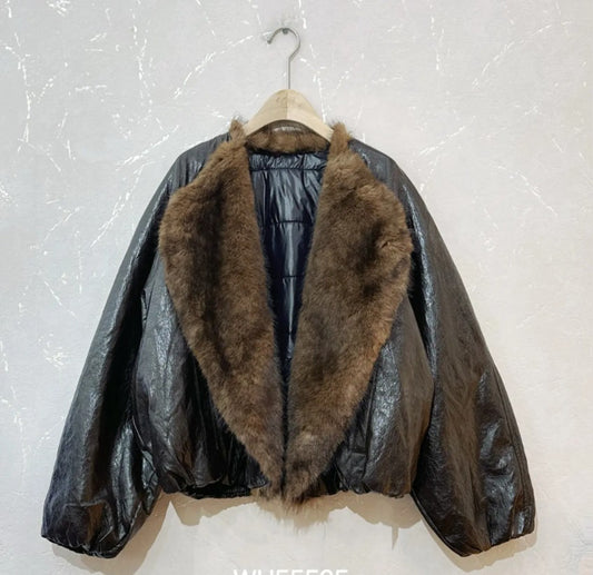 A black shiny quilted puffer jacket with a large brown faux-fur collar, hanging on a wooden hanger against a light textured wall.