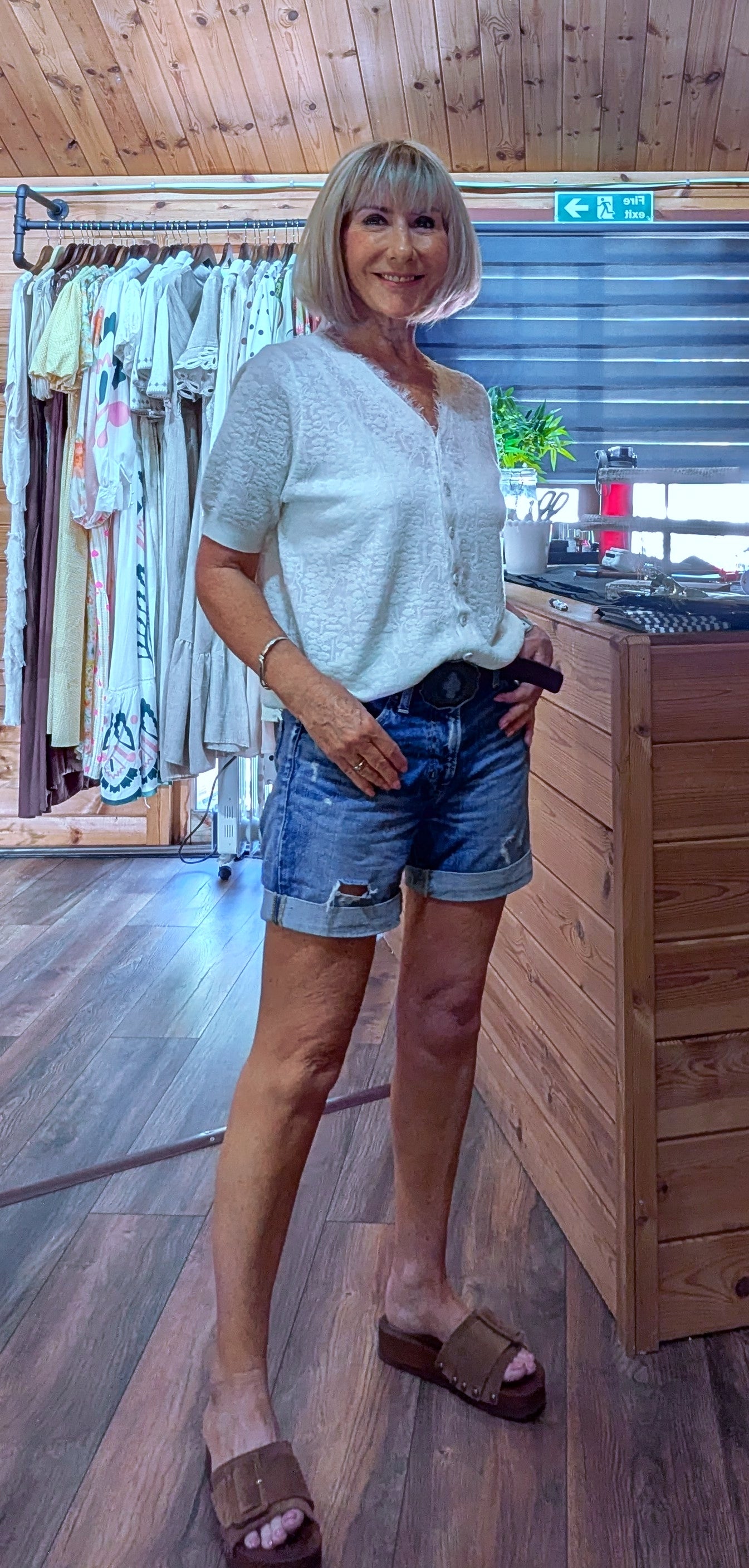 Woman wearing the Adeline cream viscose knit top with a V-neck, button front and short sleeves, styled with denim shorts. One size fits UK 8–14.