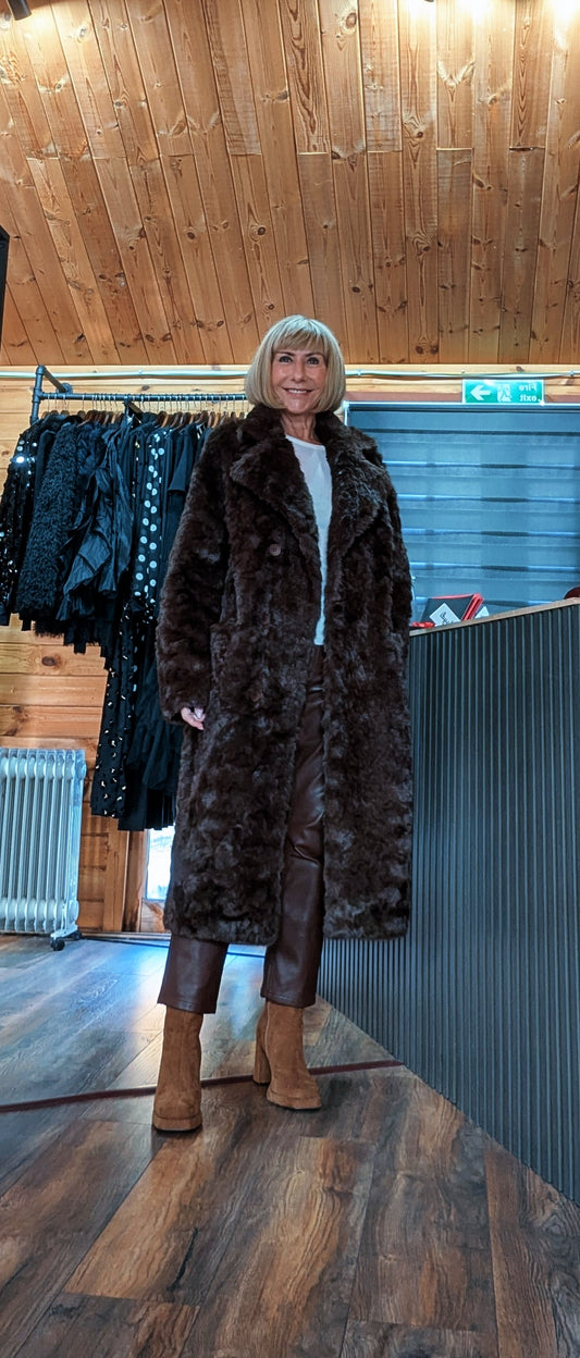 Full-length front view of Nova chocolate faux fur coat worn over a black outfit in the Ditsydi shop.