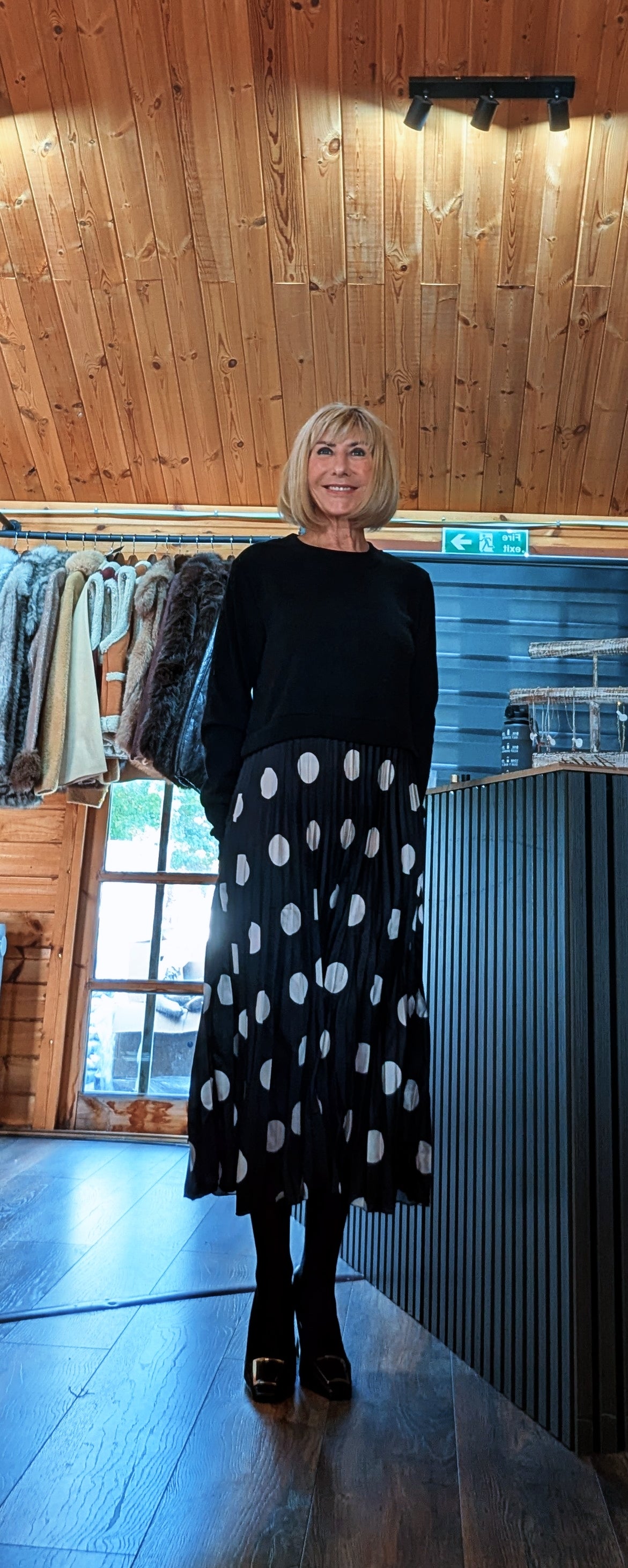 Front view of Hettie styled with a black shoulder bag and boots, with Di standing with crossed feet.