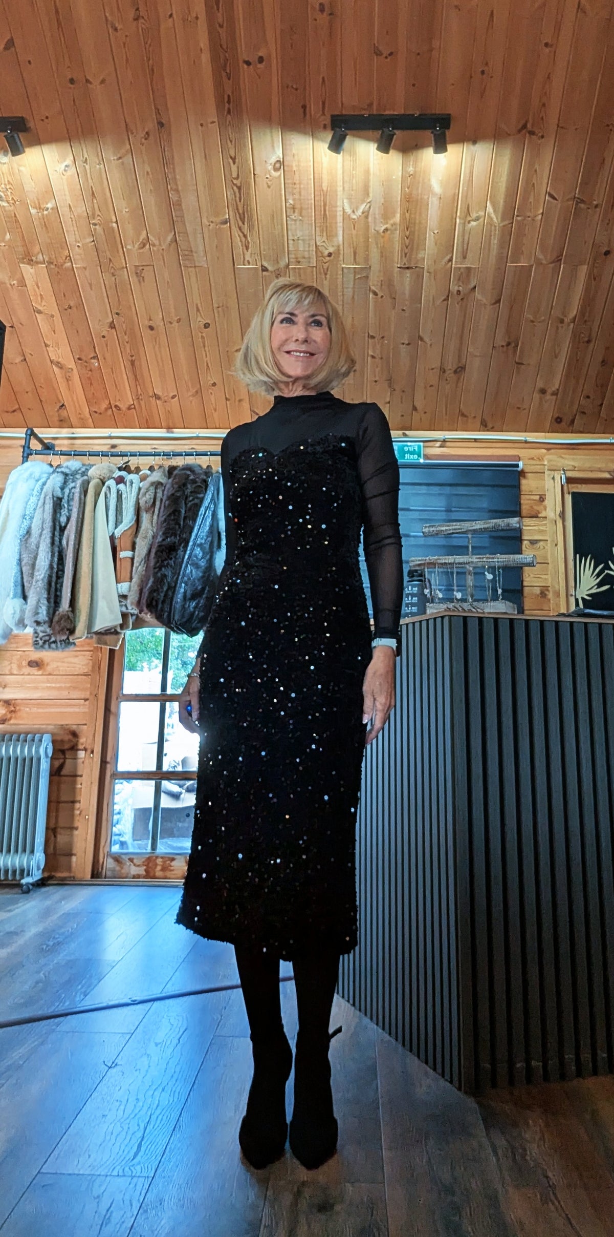 Angled front view of the Audrey sequin dress with crossed feet and a black shoulder bag.