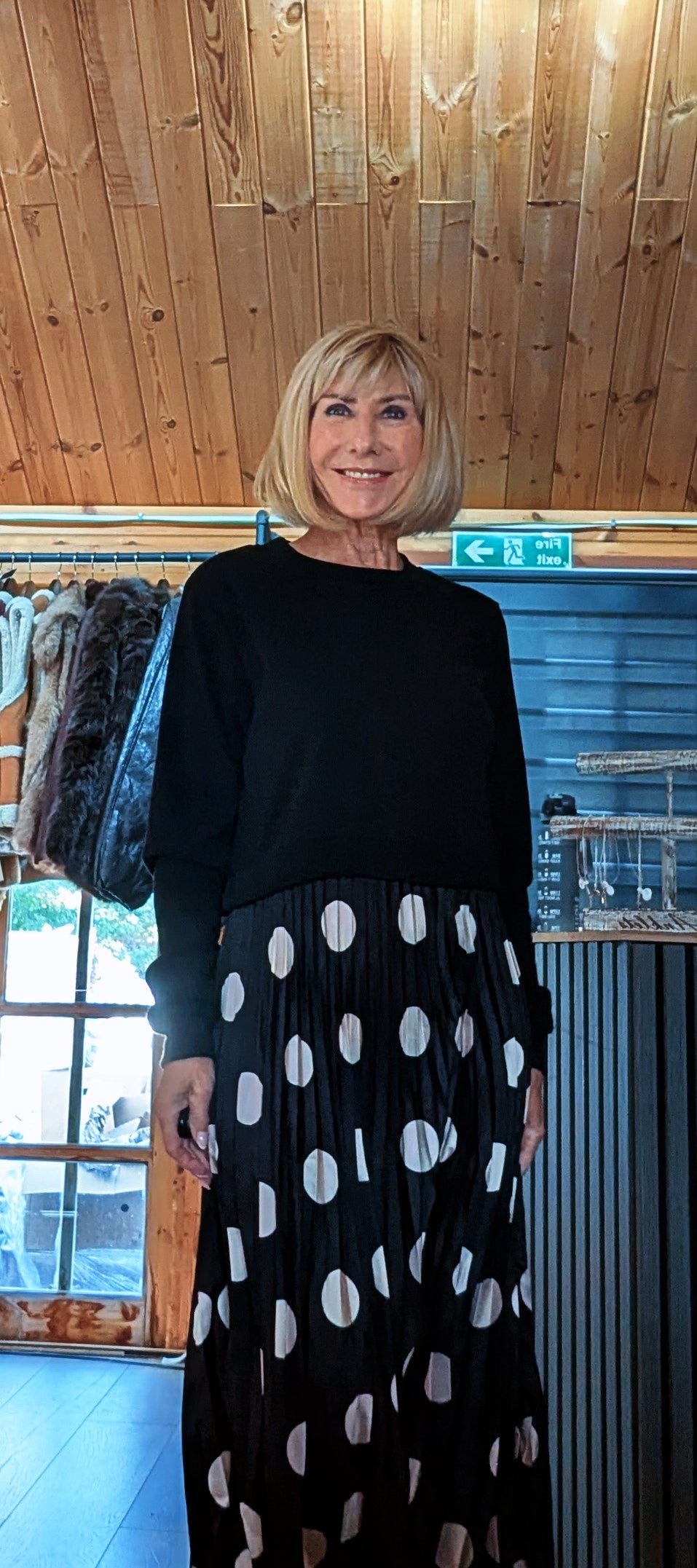 Closer view of Hettie showing the round neckline, long black sleeves and spotted pleated skirt.