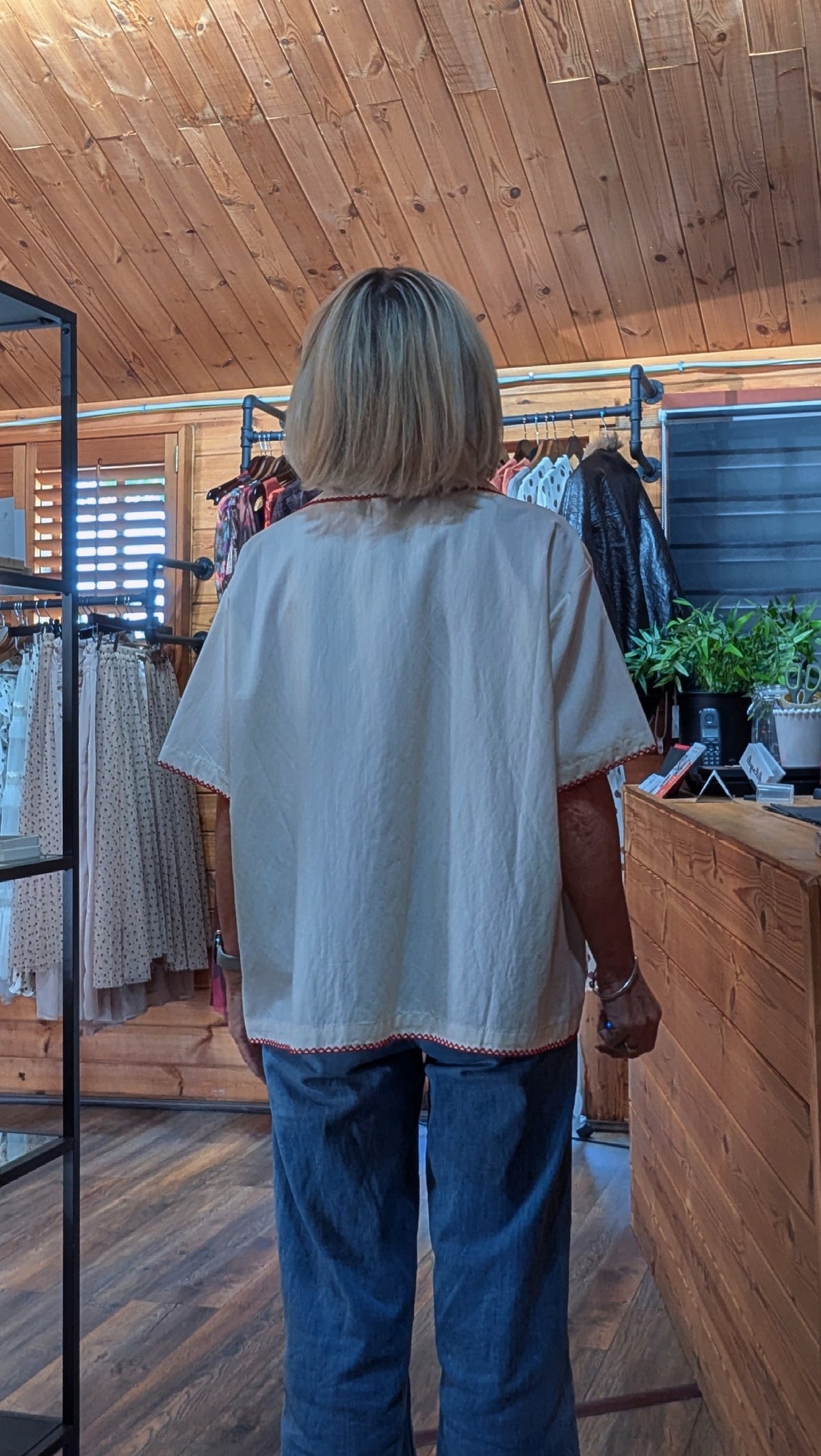 Bernadette viewed from behind wearing an oversized off-white short-sleeve shirt and blue jeans inside a boutique.