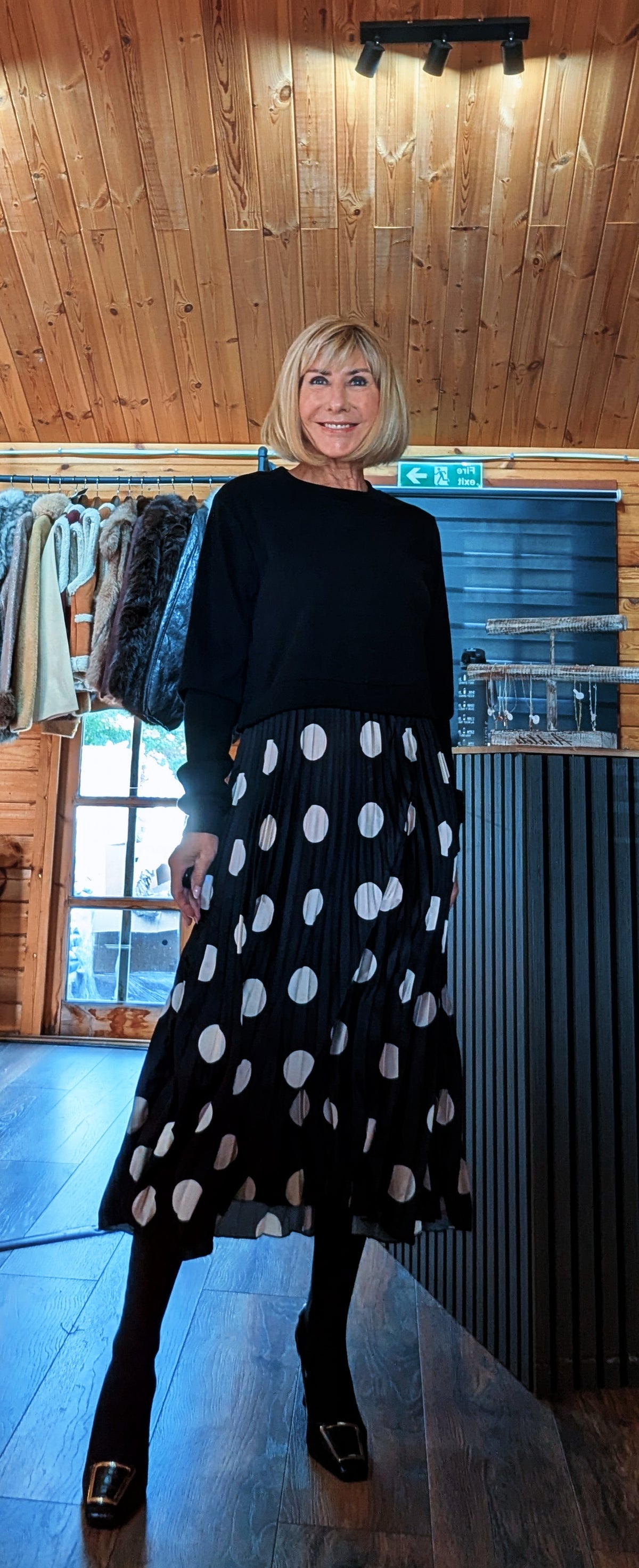 Hettie black and white spotted midi dress shown at an angle with black tights and buckle boots.